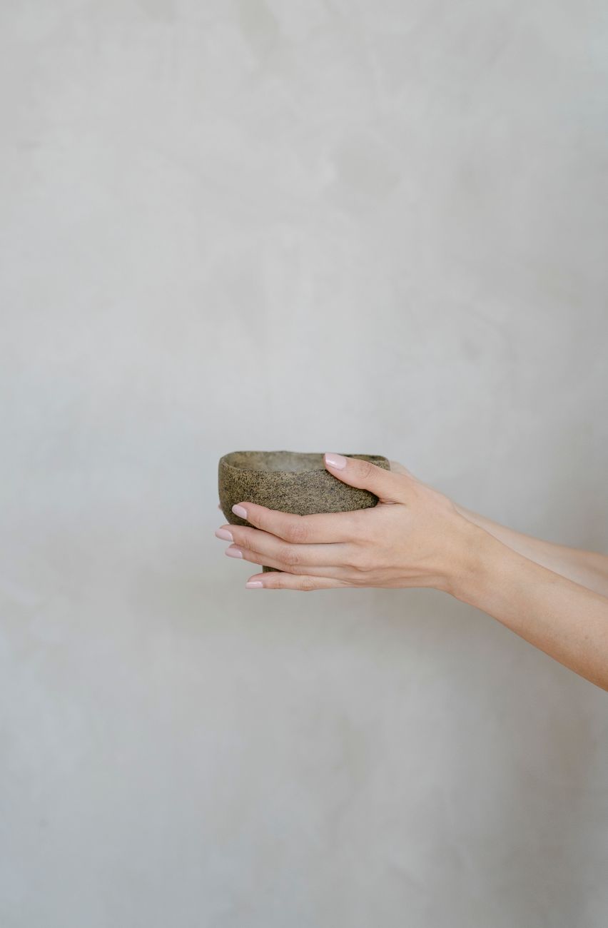 A pair of hands cradling a handmade stoneware bowl against a soft grey background — an object filed by its maker's mark.