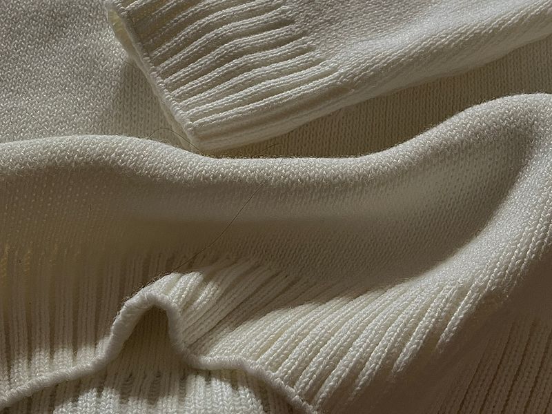 Detailed close-up of a cream wool knit showing dense traditional stitch structure — the heirloom grade of a traceable merino garment.