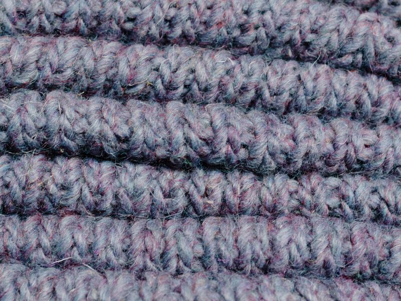 Close view of soft hand-knitted wool fabric showing fine yarn structure — the texture grade of an entry midweight merino knit.