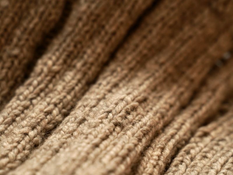 Macro view of beige woolen fabric showing fine fiber texture — the midweight grade of a core-spun merino knit.