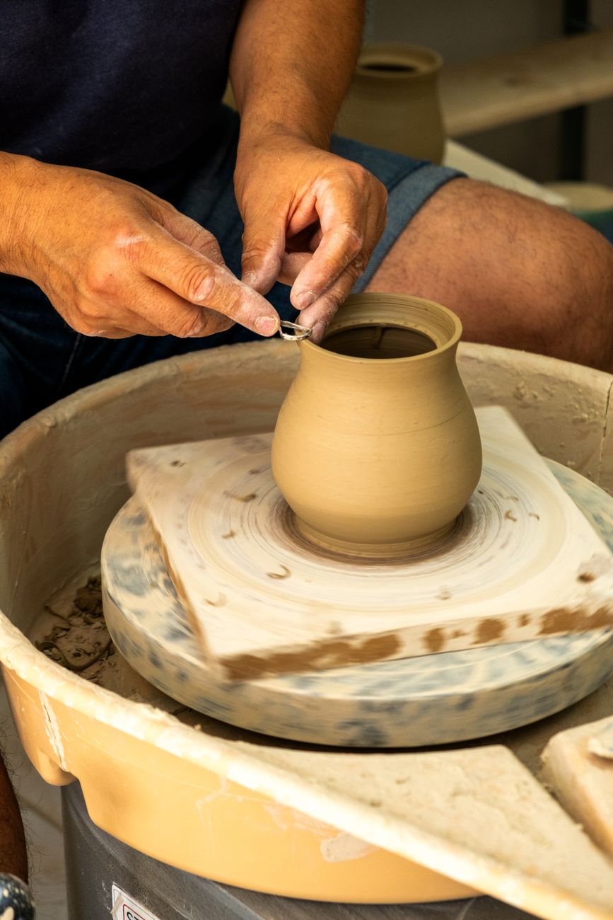 Hands shaping clay on a spinning wheel — the working posture of a British studio potter, cataloged at the moment the form is set.