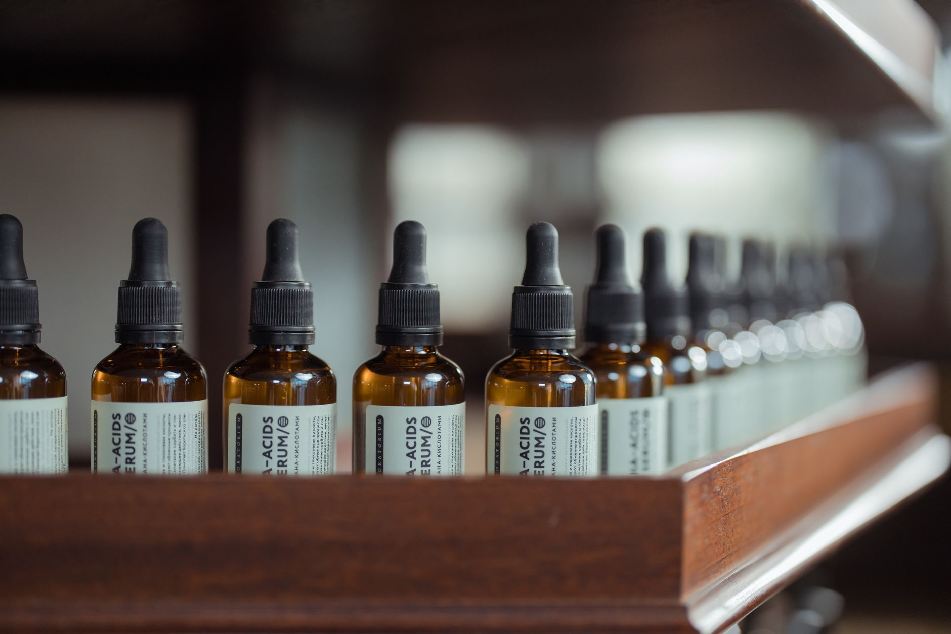 A row of amber glass dropper bottles on a wooden apothecary shelf — the specimen view of French pharmacy skincare filed by spring source and active ingredient.
