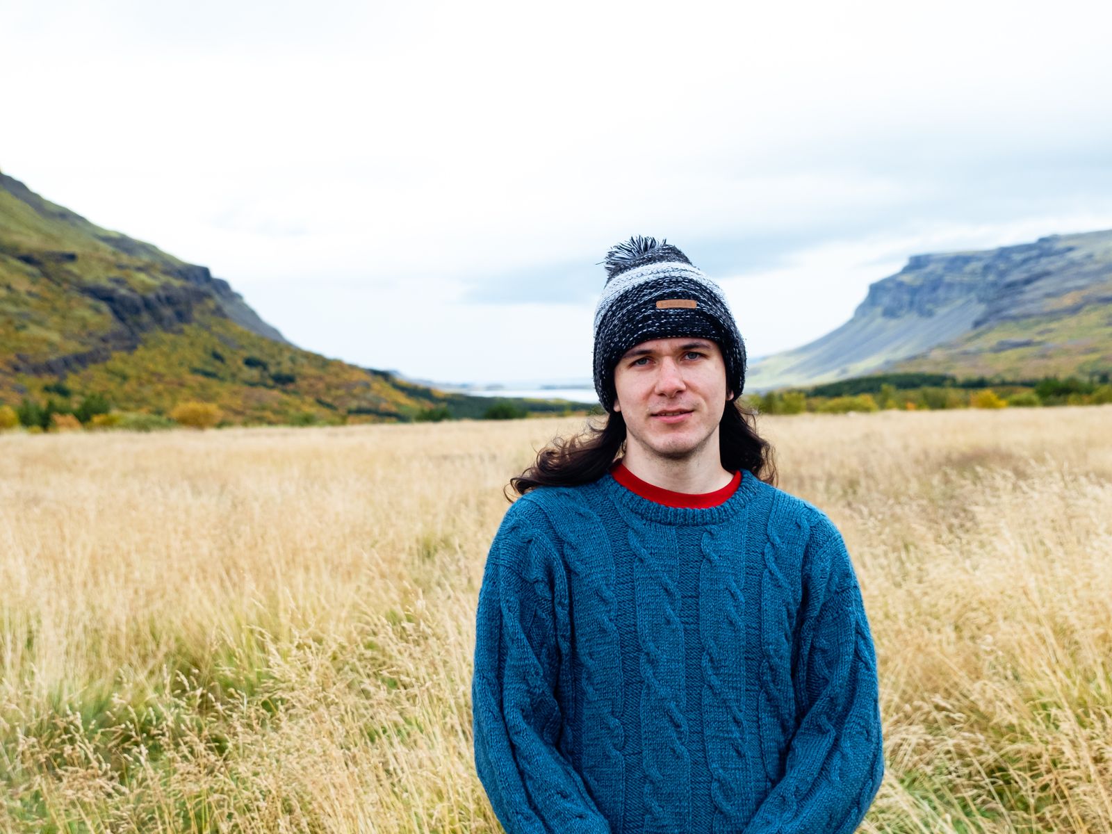 A man in a knit wool sweater standing in a mountain field in cold light — the specimen view of merino worn as the working layer it was designed for.