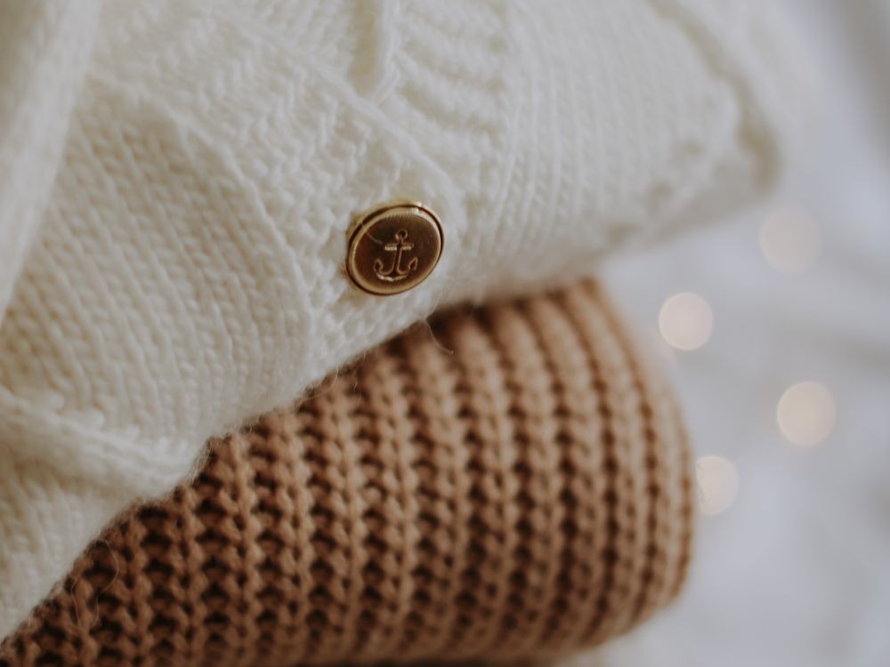 A stack of folded neutral-tone knit sweaters — base layers stored rolled and folded between seasons.