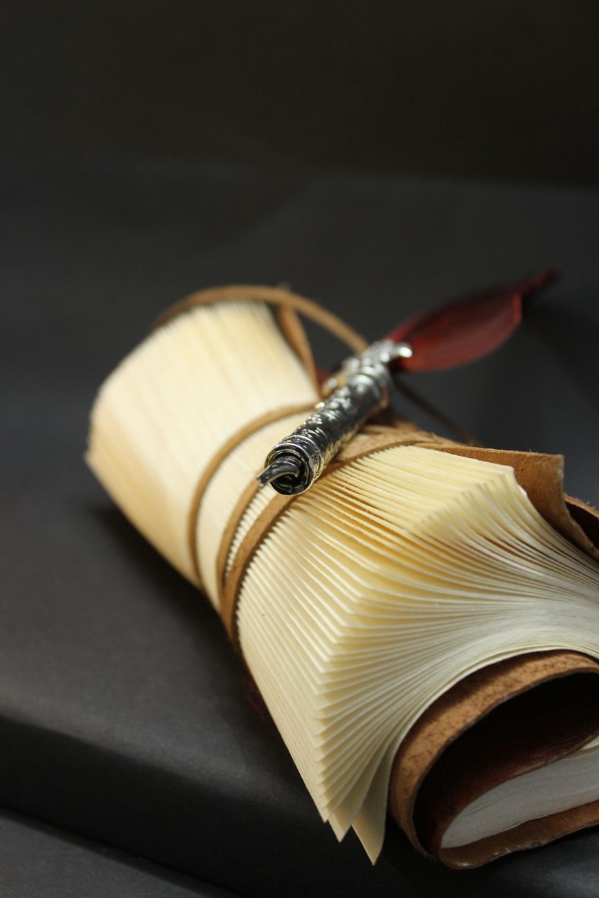 A leather notebook cover open on a desk with a silver fountain pen — the daily-use position that reveals whether the cover lies flat after two years.