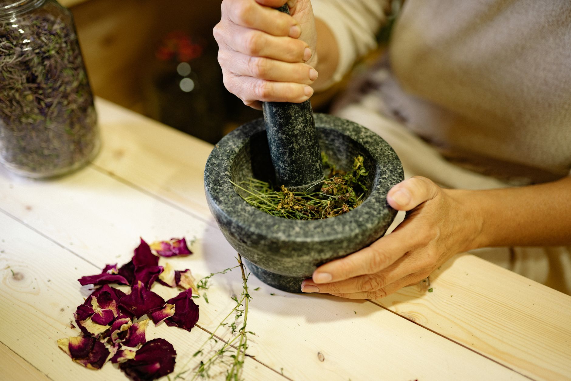 Hands grinding dried rose petals in a stone mortar and pestle — the botanical apothecary tradition that French pharmacy skincare inherits.