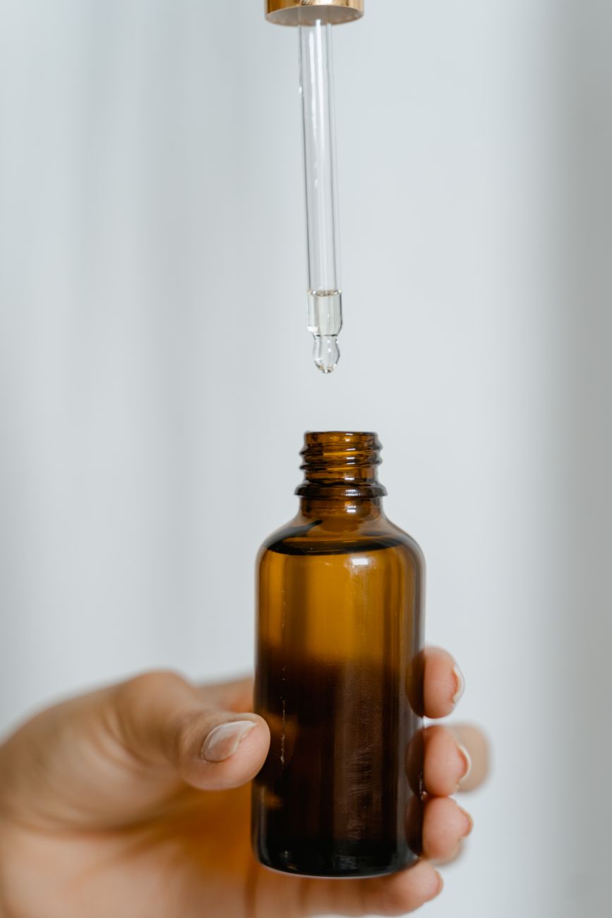 A hand holding an amber dropper bottle against a white ground — the moment before a single-active serum is applied, when concentration and vehicle are still on the label.