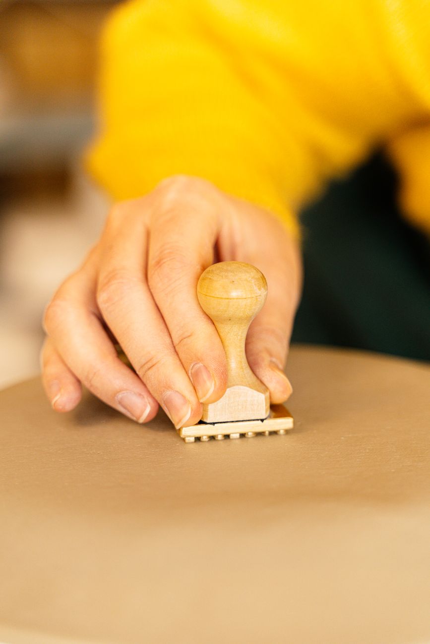 A hand pressing a wooden stamp into wet clay — the maker's mark being applied at the base, which is the first thing I check before an entry enters the catalog.
