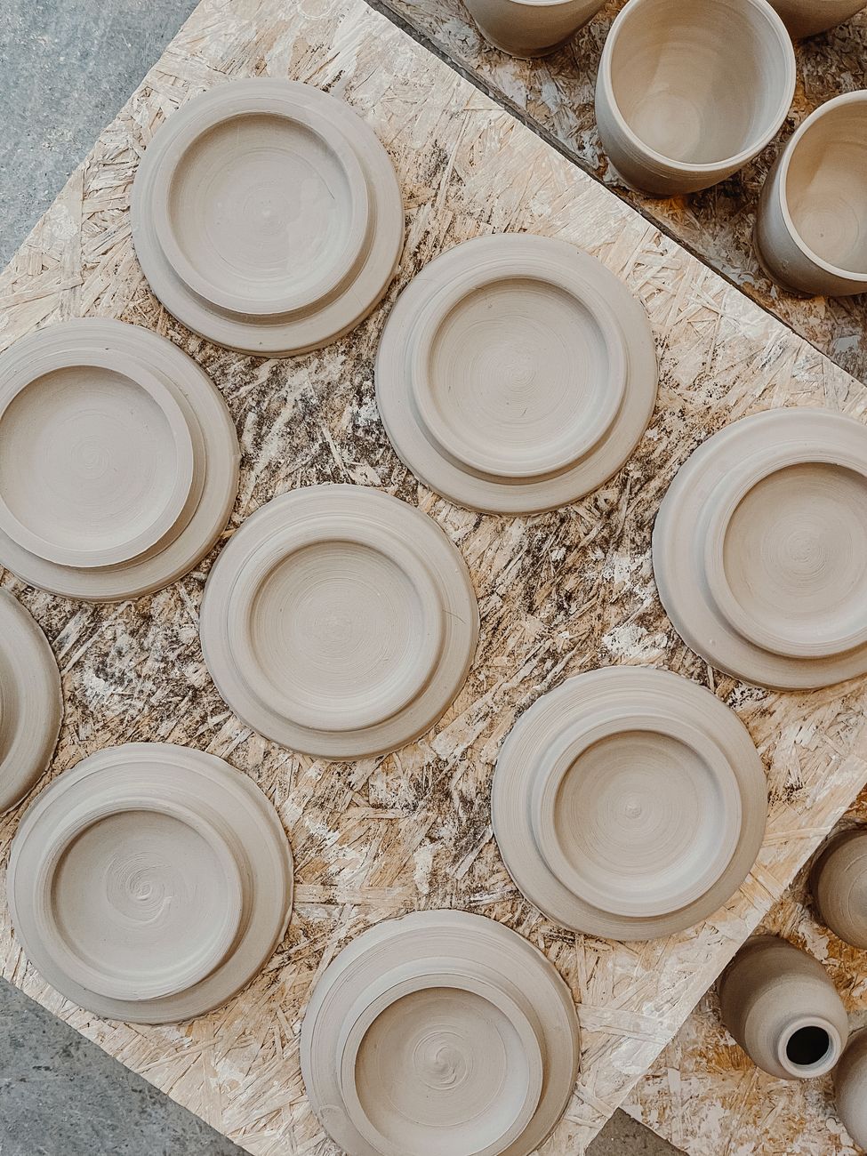 An arrangement of handmade clay plates on a wooden table — the working stoneware set, filed and ready for use.